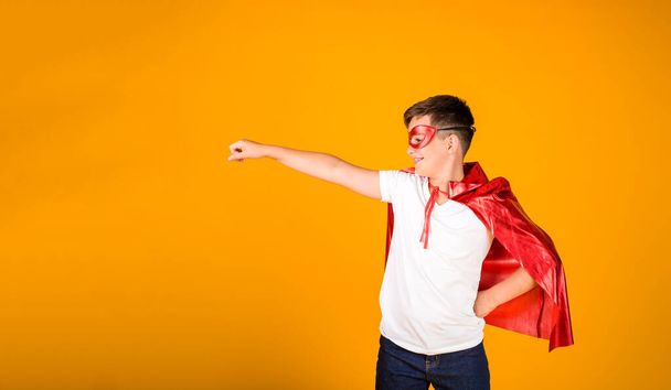 a boy in a hero costume and a mask stands on a yellow background with a place for text - Foto, Bild