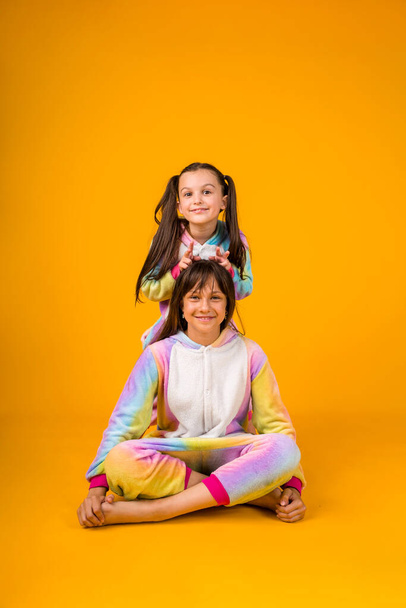 beautiful girls in plush pajamas are playing on a yellow background with a place for text - Foto, Imagem