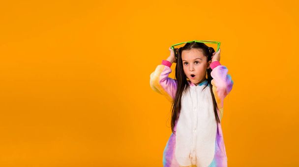 a surprised girl in a plush jumpsuit and large glasses on a yellow background with a place for text - Foto, afbeelding