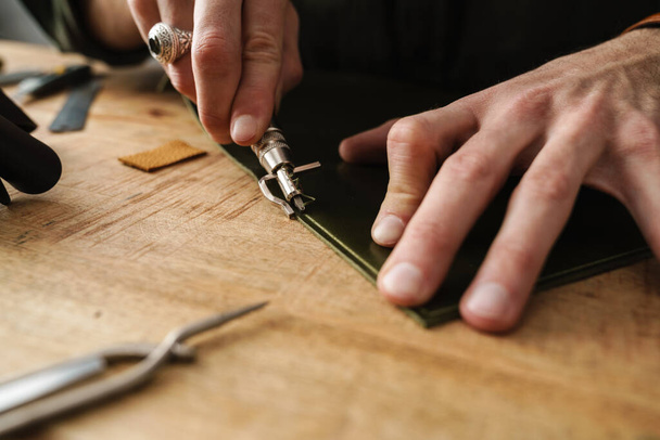 Artisan blanc travaillant avec le cuir à la table en bois dans l'atelier - Photo, image