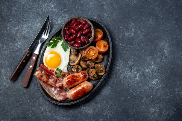English breakfast with fried eggs, bacon, sausages, beans, toasts on black background - Foto, Imagem