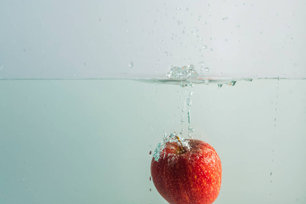 Close up view of red apple falling in water on  background.  Gorgeous backgrounds. - 写真・画像