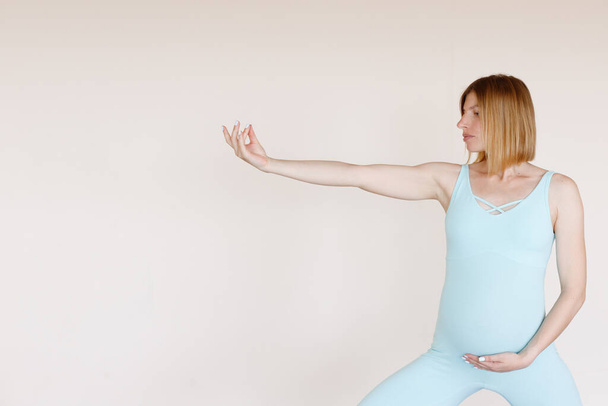 mujer embarazada en prácticas de traje de yoga sobre un fondo beige - Foto, Imagen