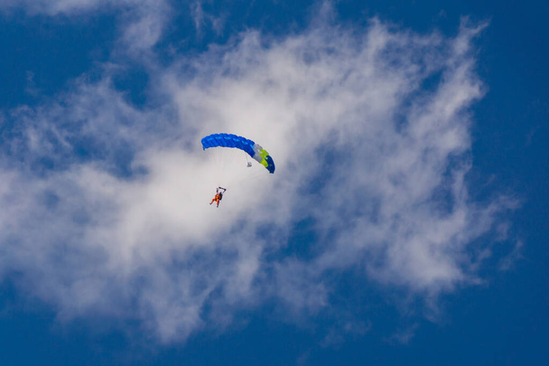 Ejtőernyős az ejtőernyő kék lombkoronája alatt a kék ég és a fehér felhők ellen. - Fotó, kép