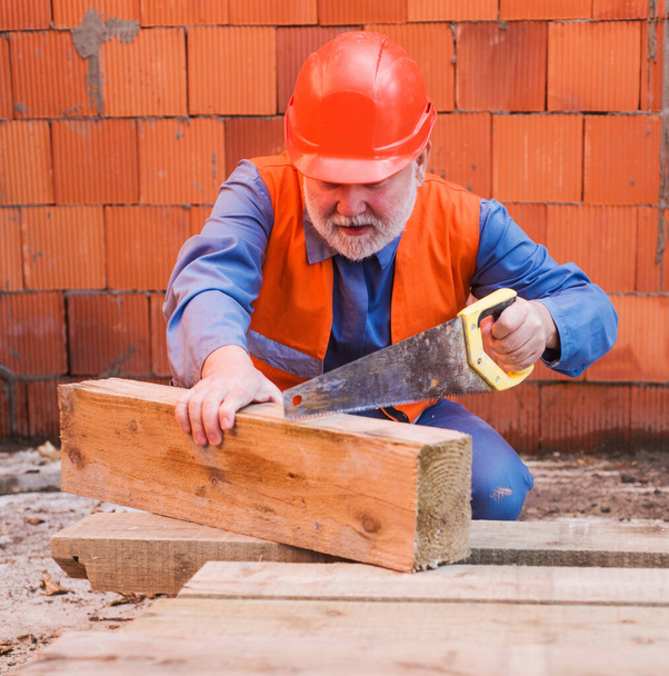 Costruttore in casco protettivo tagliere legno con sega. Carpentiere operaio edile professionista in cappello duro. - Foto, immagini