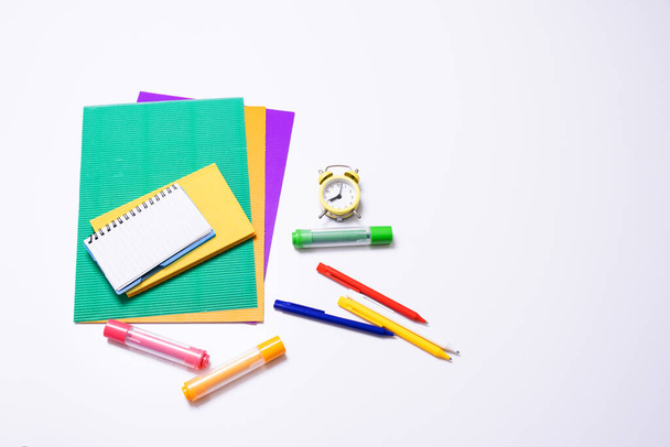 Макет школьных принадлежностей. Цветной картон, блокнот, будильник, карандаши для рисования и ручки на белом фоне. Озил образования, возвращения в школу, предметов для творчества и обучения. Копирование пространства - Фото, изображение