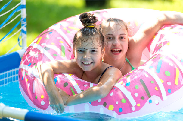 The perfect way to stay cool. Happy kids swim in donut pool float. Pool games. Poolside play. Summer - Photo, Image