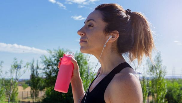 Fiatal nő vizes palackkal a kezében pihent futás után, miközben zenét hallgatott fejhallgatóval. Egészséges életmód. Szelektív fókusz. - Fotó, kép