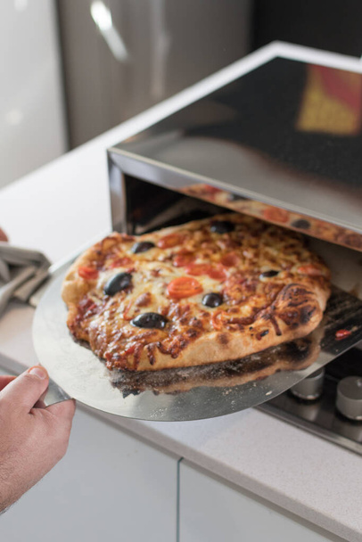 A closeup shot of a male cook hand removing baked pizza from the oven - Foto, Imagem