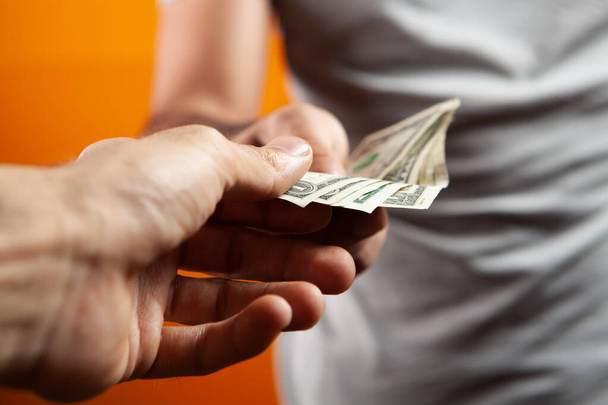 Mann hält Geld in der Hand und gibt einem anderen auf orangefarbenem Hintergrund - Foto, Bild