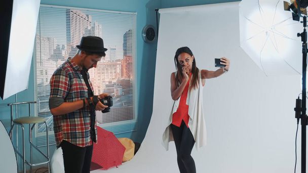 Grazioso modello nero fare selfie su smartphone durante il servizio fotografico in studio moderno
 - Foto, immagini