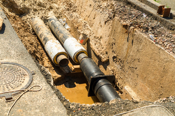 Wasserrohre im Erdgraben während der Reparaturarbeiten an den Sanitäranlagen. Reparatur einer Wasser- oder Gasleitung - Foto, Bild