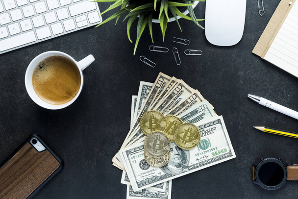 A top view of a black working desk with American banknotes, bitcoins and a cup of coffee - copy space - 写真・画像
