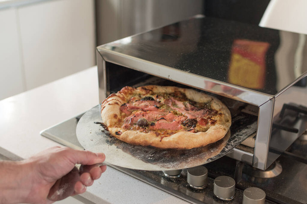 Un primer plano de un cocinero masculino retirando la pizza al horno - Foto, imagen
