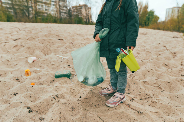 Close-up van kind het oprapen van plastic afval op het zandstrand - flessen, dozen en rietjes. - Foto, afbeelding