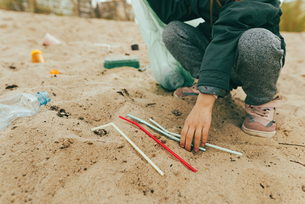 Close up de criança pegando lixo plástico na praia de areia garrafas, caixas e palhas. - Foto, Imagem
