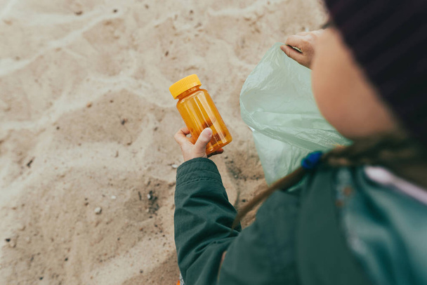 Крупним планом дитина збирає пластикові сміття на піщаному пляжі пляшки, коробки та соломинки
. - Фото, зображення