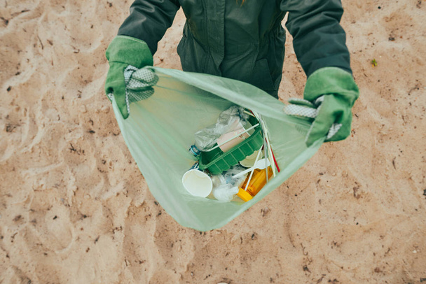 Közelkép a gyerek felvette műanyag szemetet a homokos parton - palackok, dobozok és szívószálak. - Fotó, kép