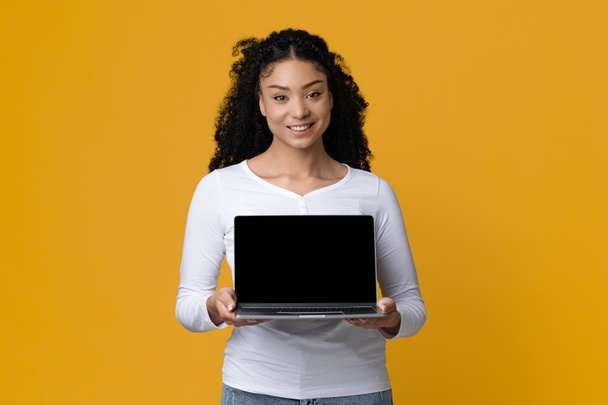 Online nabídka. Krásná usmívající se žena drží notebook s černou prázdnou obrazovkou - Fotografie, Obrázek