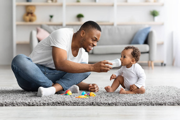Cuidando joven papá negro dando agua a su pequeño bebé en casa - Foto, Imagen