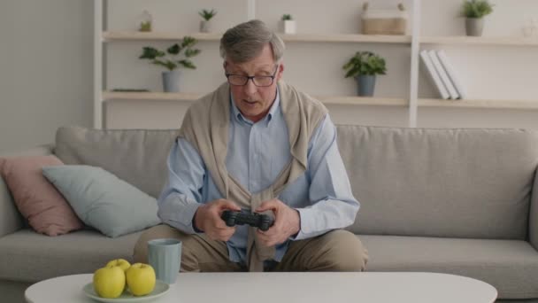 Emocjonalny starszy mężczyzna gra w gry wideo w domu z joystickiem, wygrywając, czując podekscytowany i szczęśliwy - Materiał filmowy, wideo
