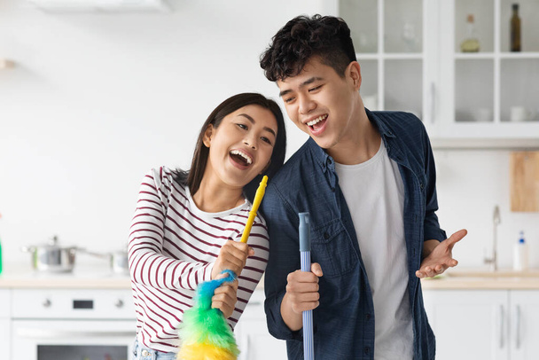 Emocional asiático hombre y mujer cantando mientras limpieza cocina - Foto, Imagen
