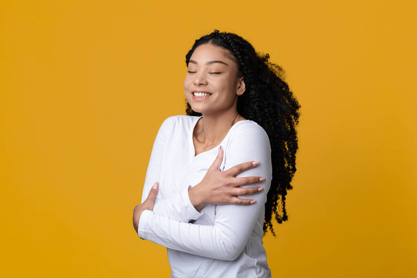 Love Yourself Konzept. Glückliche junge Afroamerikanerin umarmt sich selbst - Foto, Bild