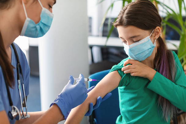 Schulmädchen erhält Coronavirus-Impfstoff-Injektion im Sitzen beim Arzt - Foto, Bild