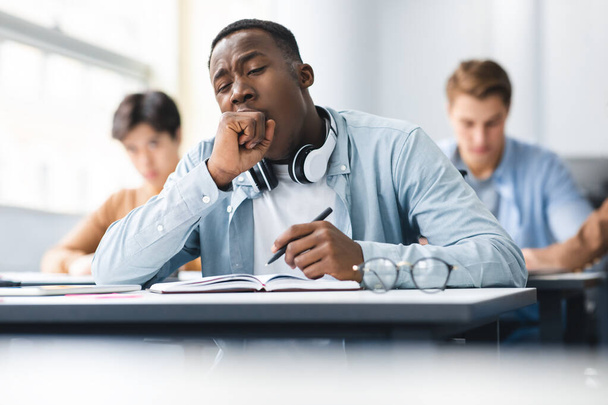 Μαύρος μαθητής χασμουρητό κάθεται στο γραφείο στην τάξη - Φωτογραφία, εικόνα