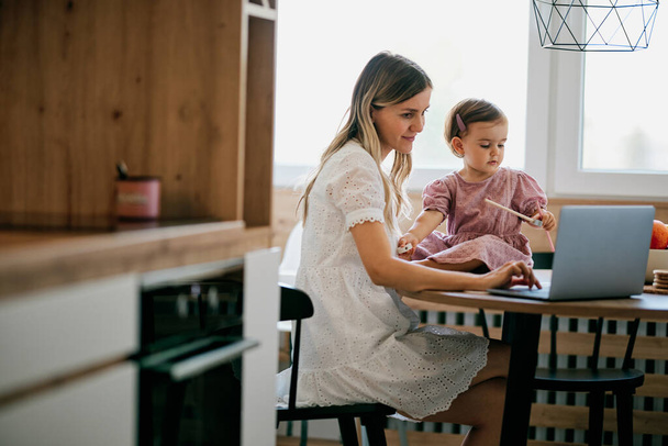 Залишайтеся вдома матері, сидячи на кухні і роблячи роботу, поки її дитина допомагає їй
. - Фото, зображення