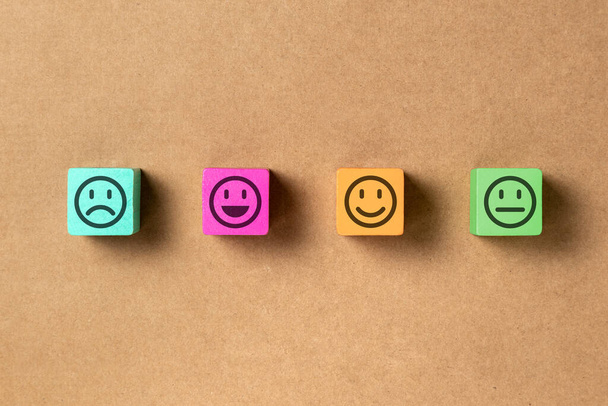 Emoticon gezichten in de kleuren houten blokken over bruin papier. Service evaluatie en tevredenheid enquête concepten. Boos, neutraal, goed humeur en gelukkig. Kopieerruimte. - Foto, afbeelding