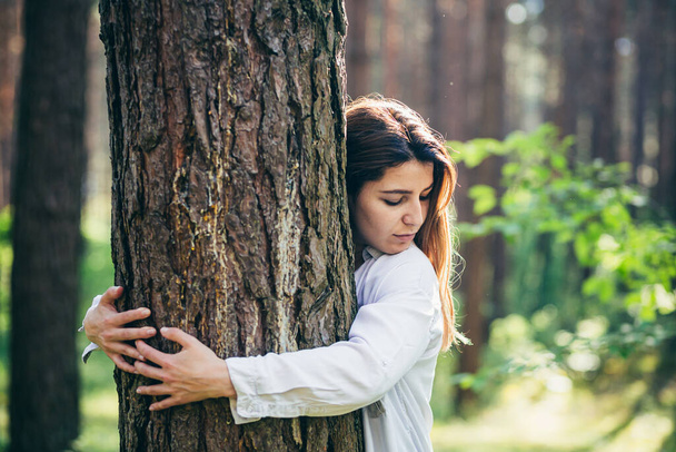 Young beautiful female volunteer hugs a tree with love in the forest - Foto, imagen