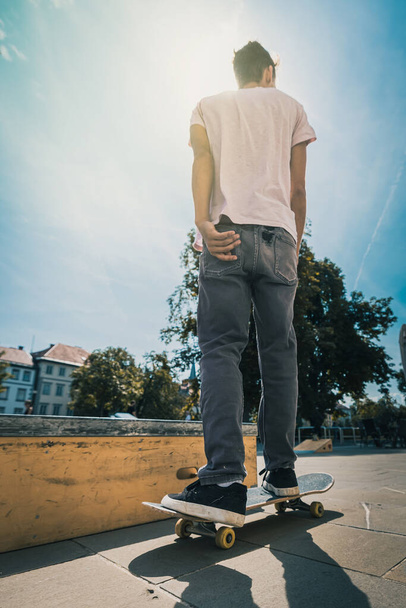 Anônimo skate boarder cavalgando longe da câmera em um belo dia ensolarado na cidade. - Foto, Imagem