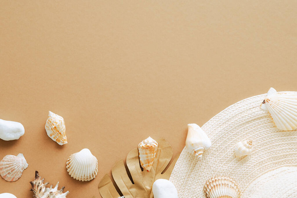 Straw beach hat, golden monstera leaf, seashells on sandy background. Summer flat lay composition. - Foto, Bild