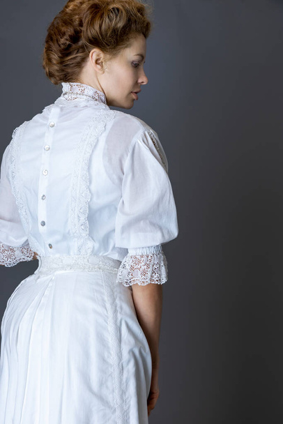 Beyaz dantelli bluz ve uzun inci kolyeli etek giyen bir Edwardlı kadın gri bir stüdyo arkaplanına yaslanmış.  - Fotoğraf, Görsel