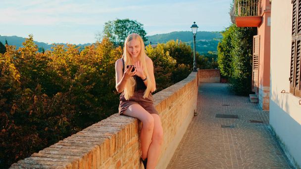 Позитивная блондинка делает видеозвонок со смартфона с места своего визита - Фото, изображение