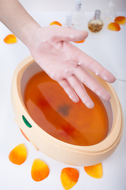 Female hand orange parrafin wax in bowl. Manicure beauty spa salon - Foto, immagini