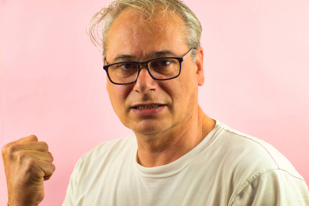 κοντινό πλάνο του ώριμου άνδρα με γυαλιά και γκρίζα μαλλιά με υψωμένη γροθιά γιορτάζει σε ροζ φόντο - Φωτογραφία, εικόνα