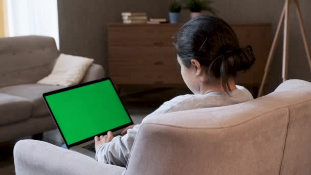 Смешанная расовая этническая женщина, лежащая дома на диване, использует ноутбук с зеленым макетом экрана. Через плечо.  - Кадры, видео
