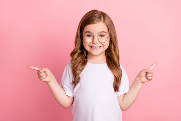 Photo of adviser little girl indicate forefingers empty space wear specs white t-shirt isolated pink color background - Foto, Imagem