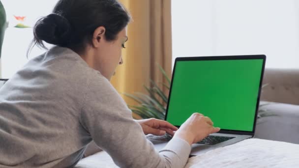 Žena na volné noze sedí na pohovce v domácí kanceláři psaní na notebooku s maketou zelené obrazovky chroma klíč - Záběry, video