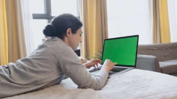 Green Screen Mock Up Girl sentado en el sofá y mirando continuamente en la pantalla del ordenador portátil en la acogedora sala de noche - Imágenes, Vídeo