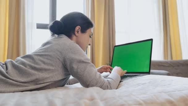Green Screen Mock Up Girl sentado en el sofá y mirando continuamente en la pantalla del ordenador portátil en la acogedora sala de noche - Imágenes, Vídeo