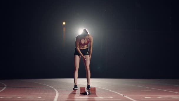Uma jovem está sozinha no estádio de atletismo e se preparando para a corrida. Preparação para o sprint. Concentração e preparação psicológica para competições em câmara lenta - Filmagem, Vídeo