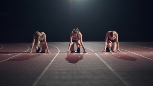 Bir dizi koşucu kadın yarışa başlamadan önce başlangıç pozisyonunda çömelir. Dişiler, stadyumdaki koşu ayakkabılarıyla başlar. Başlangıçtan başlayarak karanlıkta spot ışıkları yavaş çekimde olur.. - Video, Çekim