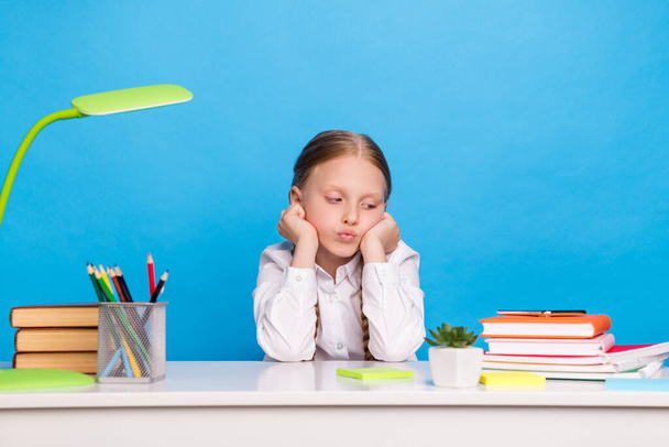 Photo portrait schoolgirl sitting at desk near book pile bored tired upset isolated pastel blue color background - Foto, imagen