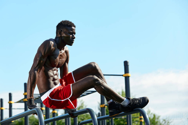 Musta nuori mies treenaa puiston epätasaisissa baareissa, crossfit-konsepti, afrikkalainen amerikkalainen mies tekee harjoituksia kaduilla, urheilukentillä - Valokuva, kuva