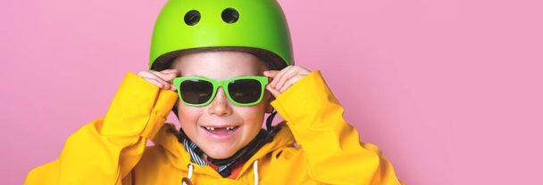 Retrato del niño rubio en casco de seguridad está listo para montar en scooter. El niño está en equipos de protección de calidad para la seguridad. Gafas de sol y abrigo amarillo. Siete años. Cara sonriente. Alumno de la escuela - Foto, Imagen