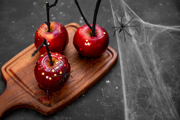  Κόκκινα μήλα σε καραμέλα με εορταστική διακόσμηση Halloween, ένα πρωτότυπο κέρασμα για ένα γιορτινό τραπέζι Halloween διακοσμημένο με αράχνες και ιστούς αράχνης, αντίγραφο χώρου για κείμενο - Φωτογραφία, εικόνα