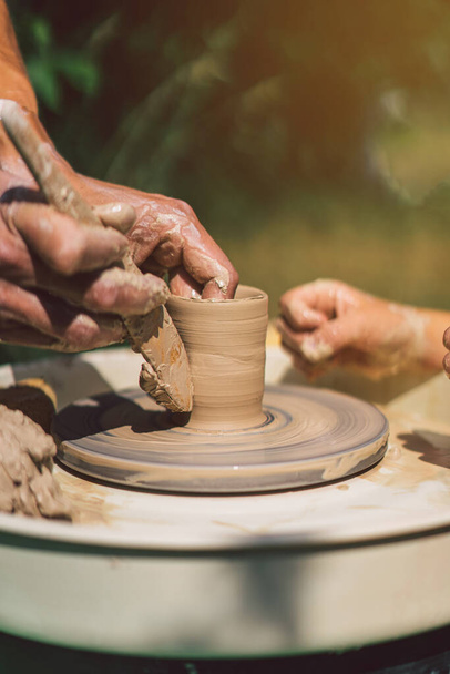 Potter making a clay object on pottery wheel in outdoors. Craftsman moulding clay with hands on pottery wheel - Photo, Image